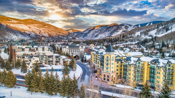 A snow-covered town with a prominent yellow building featuring multiple floors and a tower. - Luxury Duplex | Air Conditioning | Private Hot Tub | On Bus Loop (Avon)