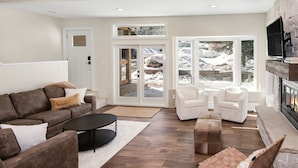 A modern living room with a brown leather sofa, white armchairs, a black coffee table, and a fireplace. - Luxury Duplex | Air Conditioning | Private Hot Tub | On Bus Loop (Avon)