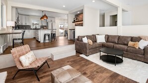 A modern living room with a sectional sofa, a coffee table, and a chair with a fluffy pillow. - Luxury Duplex | Air Conditioning | Private Hot Tub | On Bus Loop (Avon)