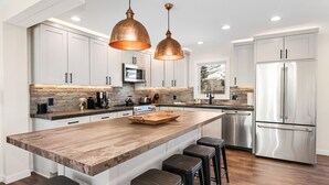 A modern kitchen with a large island, stainless steel appliances, and pendant lighting. - Luxury Duplex | Air Conditioning | Private Hot Tub | On Bus Loop (Avon)