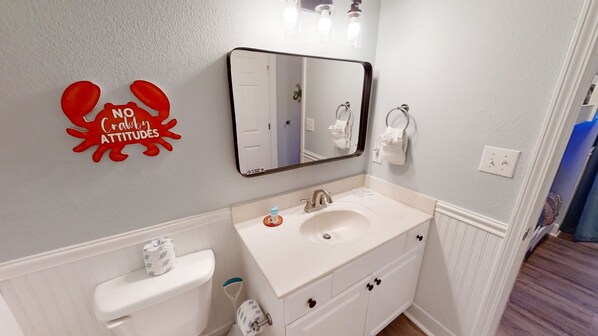 Une salle de bain avec un lavabo blanc, des toilettes, un miroir et un élément de décoration murale rouge portant l’inscription : « Pas d’attitude de crabe. »