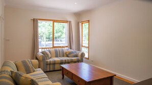 A living room with a sofa, a coffee table, and two windows with curtains.