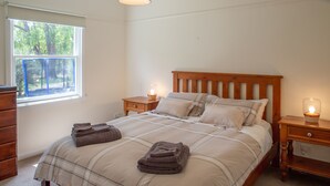 A bedroom with a bed, nightstands, a dresser, and a window with blinds.