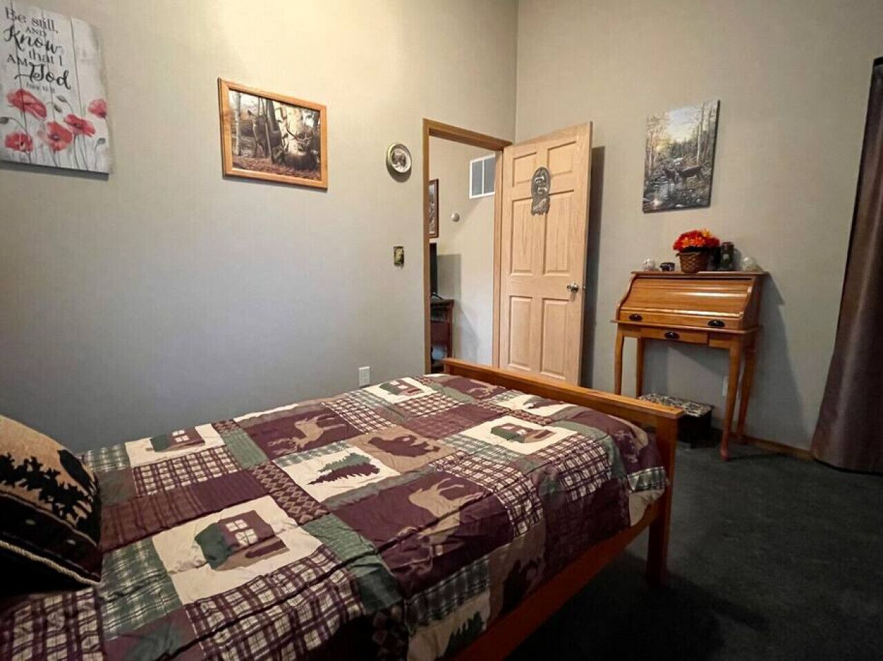 A bedroom with a bed, a wooden dresser, a door, and a wall with a framed picture.