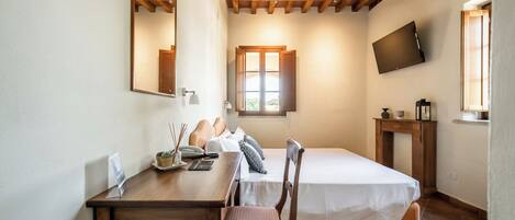 Un dormitorio con techo de madera, una cama, un escritorio con silla, un televisor y una ventana con luz natural.