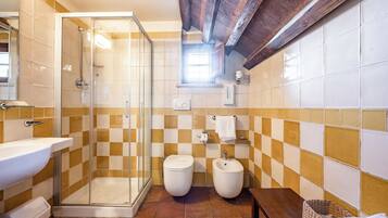 Une salle de bain avec une douche à parois de verre, un lavabo, deux toilettes et un bidet.