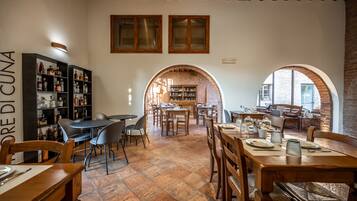 Un restaurant acollidor amb taules i cadires de fusta, una paret de maó i prestatges plens de botelles.