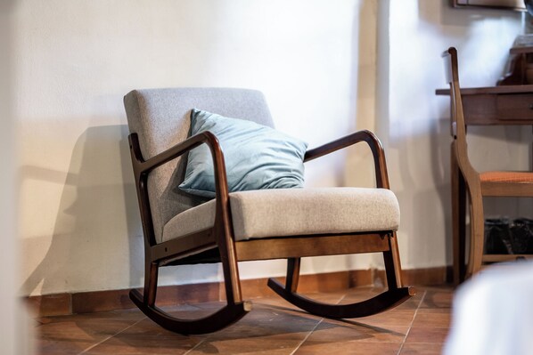 Un fauteuil à bascule avec un coussin et un oreiller, placé contre un mur dont le sol est recouvert de carreaux.