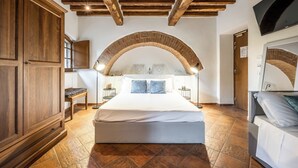 A bedroom with a large bed, wooden ceiling beams, an arched brick ceiling, and a TV on the wall. - Hotel More Di Cuna (Monteroni d'Arbia)