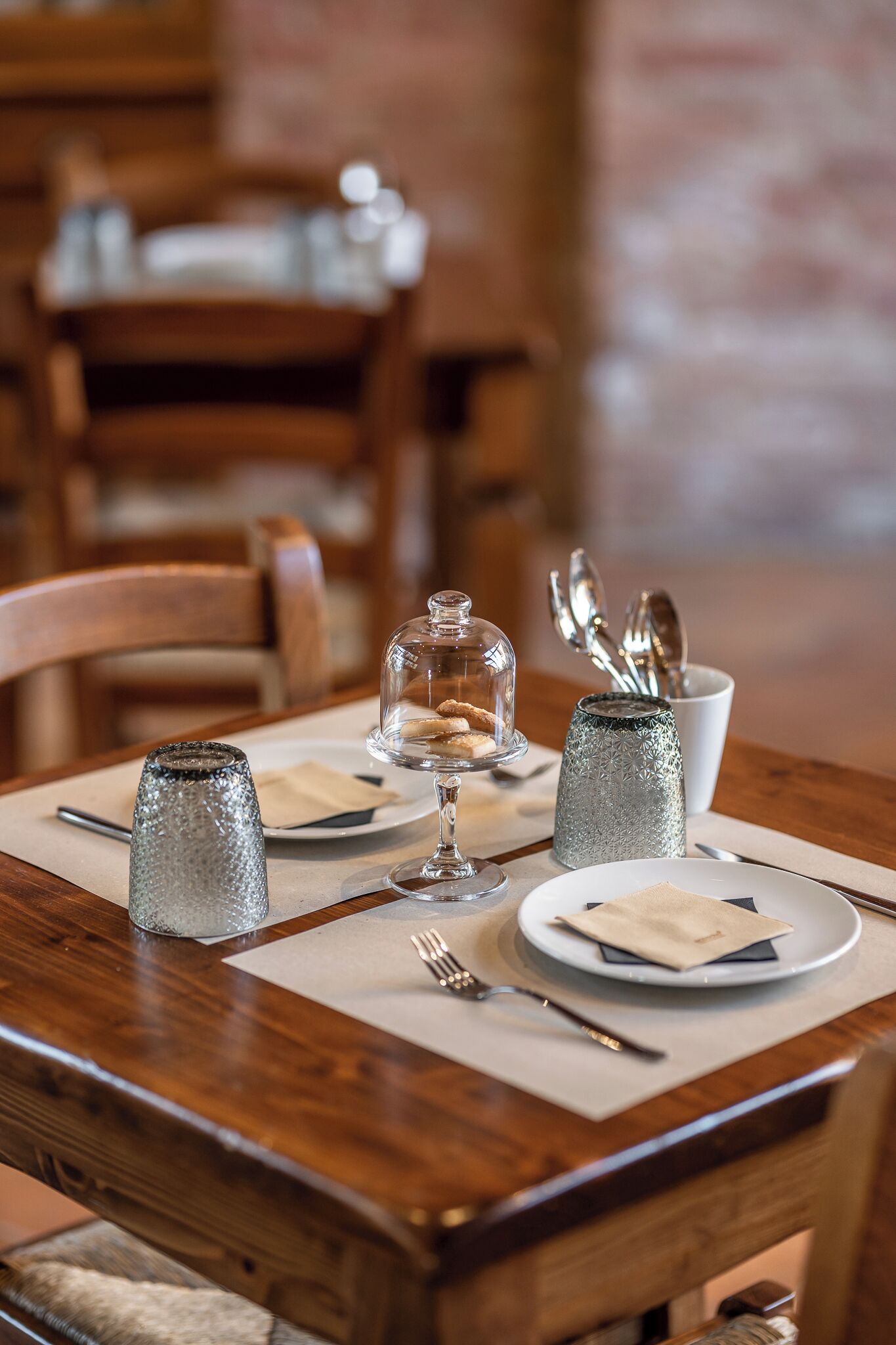 A dining table set with a glass dome dessert, a salt and pepper shaker, a glass, and a plate with napkin and cutlery.