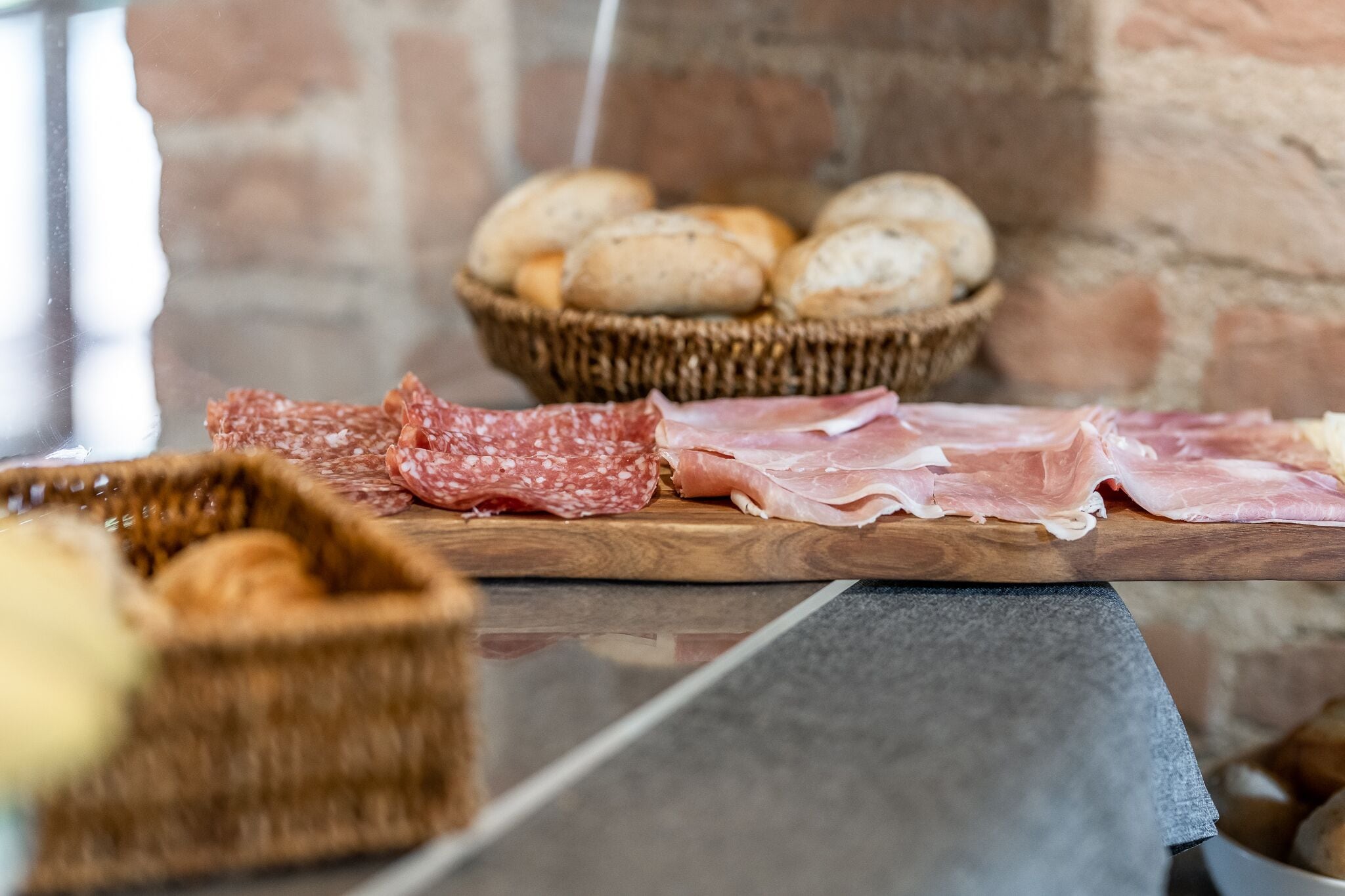 Une planche en bois garnie de différentes sortes de charcuteries et un panier de pain.