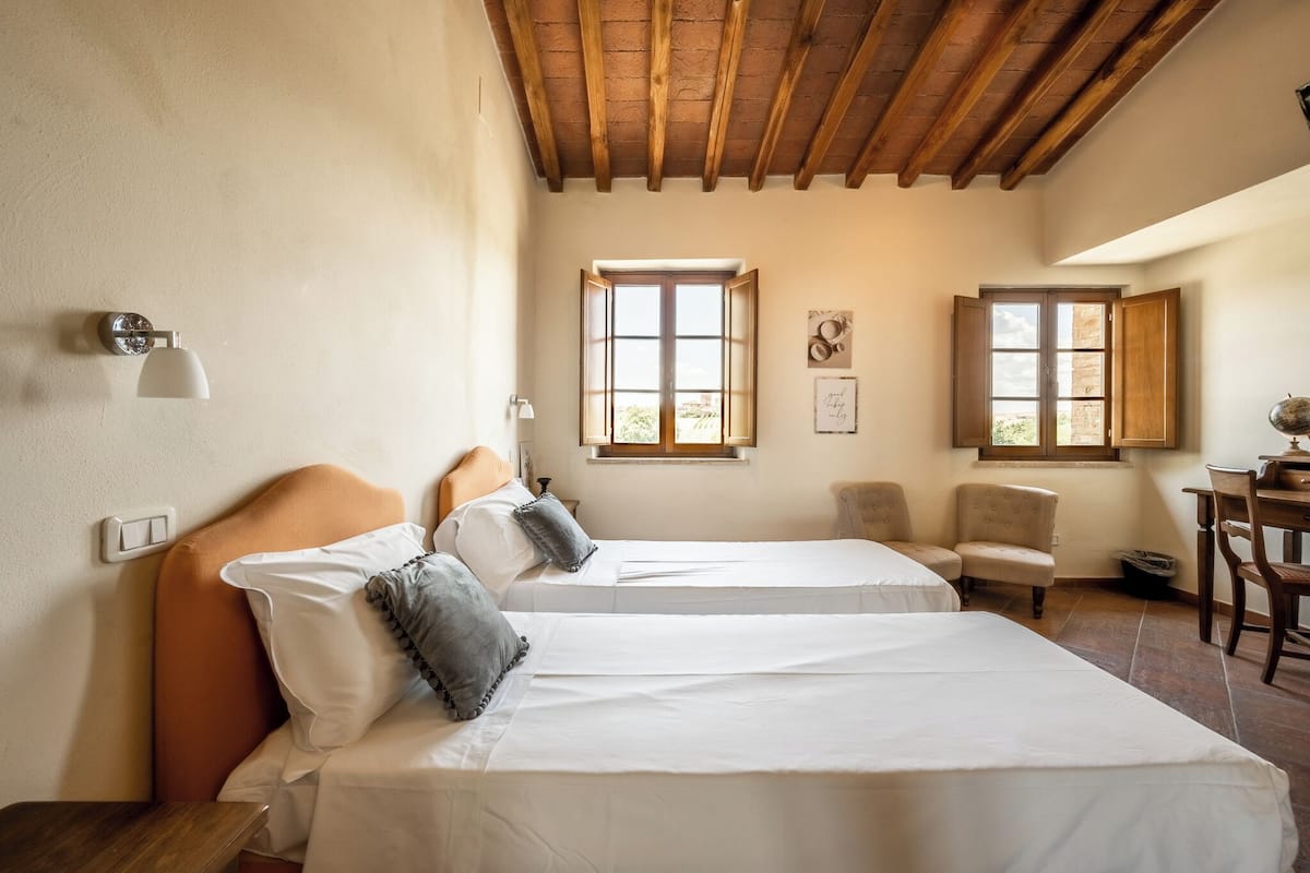 Un dormitorio con dos camas, vigas de madera, un escritorio y dos ventanas.