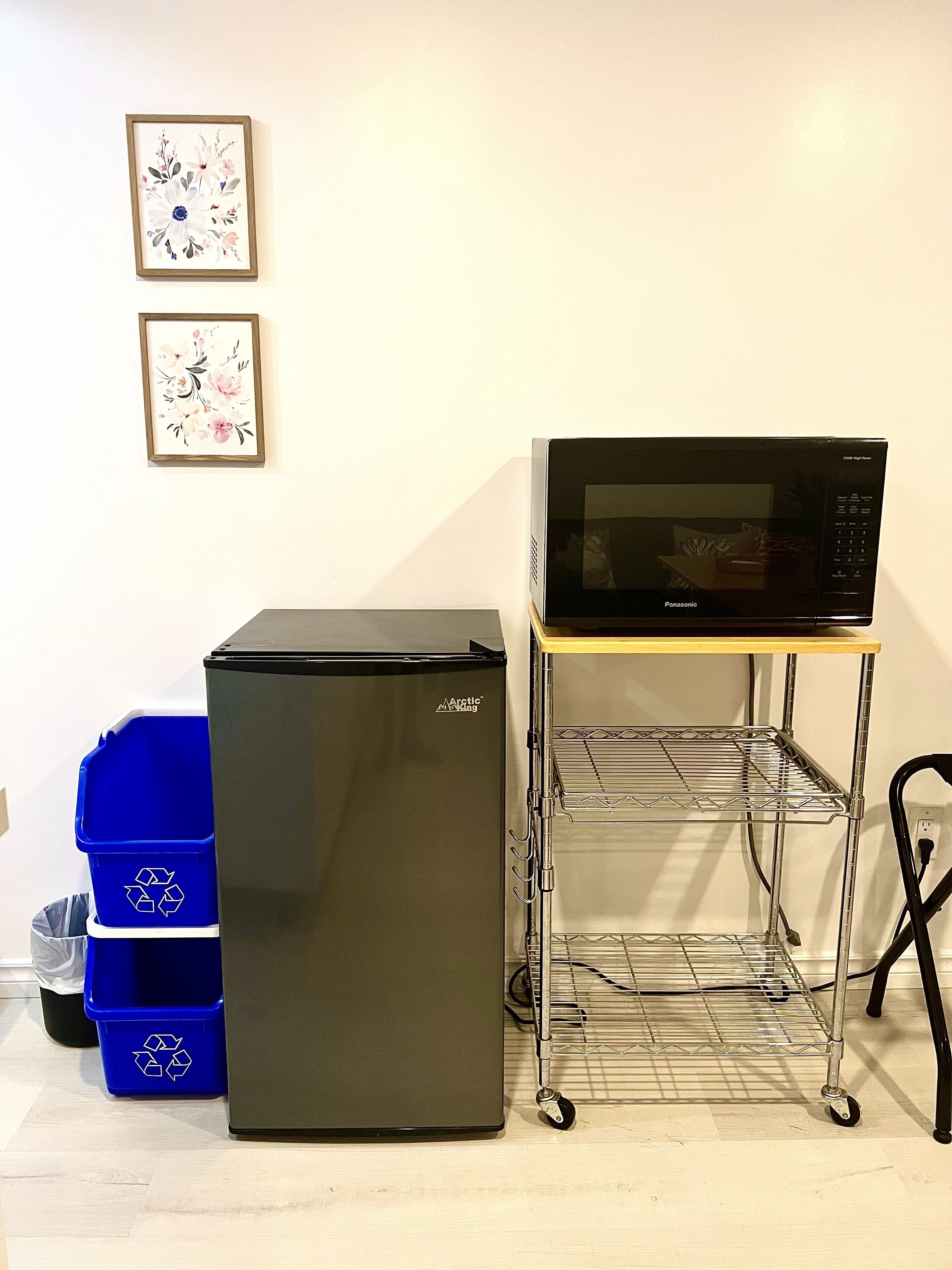 A black refrigerator, a microwave on a cart, and blue recycling bins.