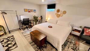 Quarto moderno com uma cama grande, uma escrivaninha e uma cadeira. Há painéis decorativos nas paredes e uma pequena planta na mesa de cabeceira.