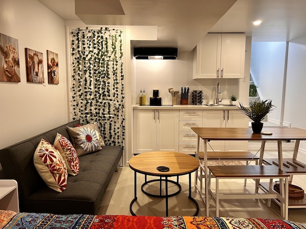 A modern living room with a sofa, a coffee table, and a dining area with a table and chairs. - The Boho Oasis: Luxurious Studio Apartment, Quiet Court, Close to All Amenities! (Windsor)