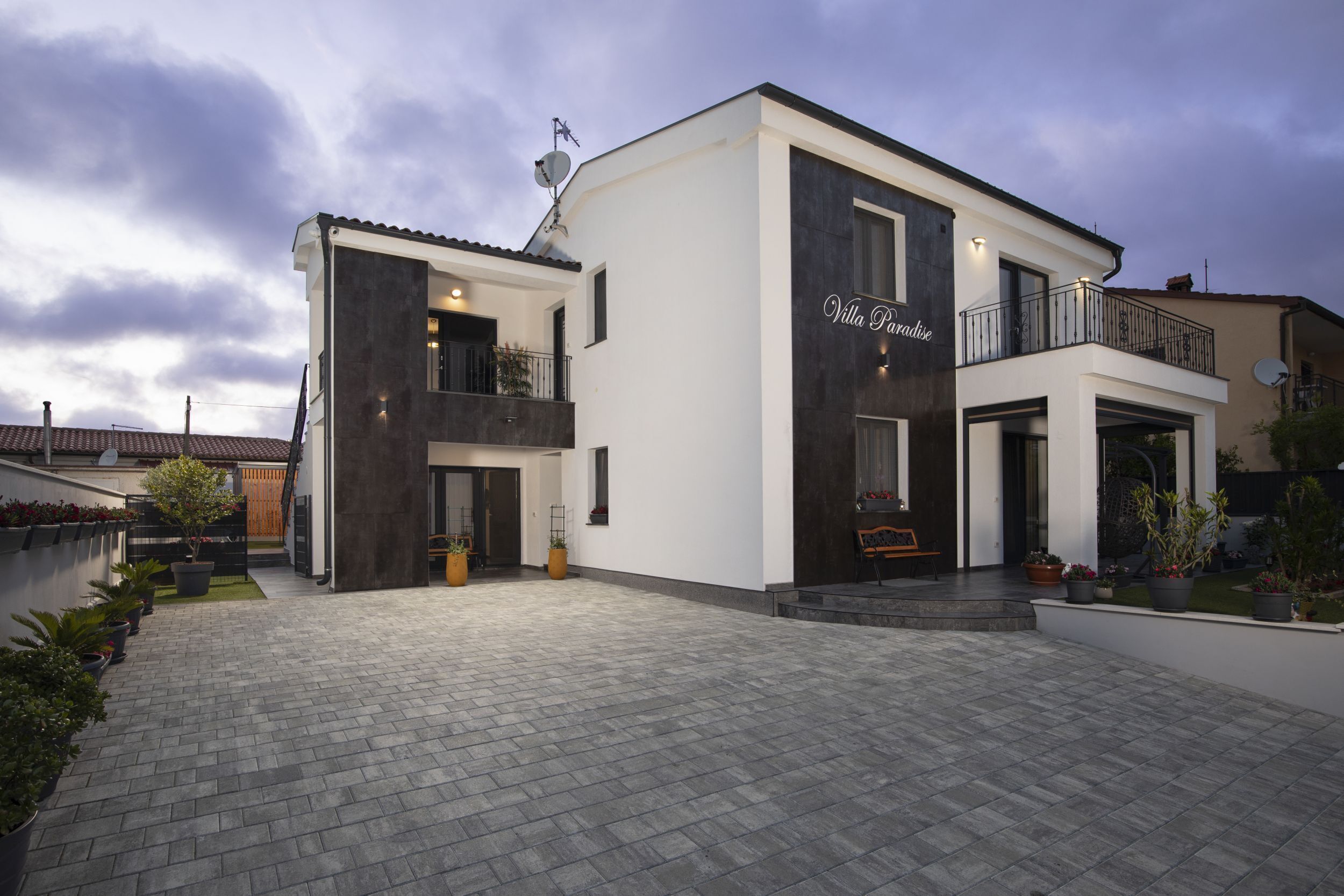 A modern villa with a two-story structure, a balcony, and a paved driveway.