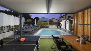 Un espace extérieur abrité comprenant une piscine, des chaises longues, une table de ping-pong et une table à manger avec des chaises.