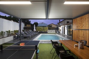 Un'area esterna coperta con piscina, sedie a sdraio, tavolo da ping pong e tavolo da pranzo con sedie.