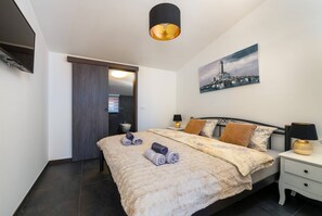 Une chambre moderne avec un grand lit, une table de chevet avec une lampe, un tableau au mur et une porte donnant sur une autre pièce.