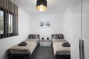 A modern bedroom with two beds, a nightstand, a lamp, and a painting on the wall.