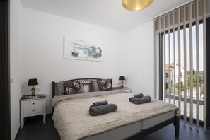 Una camera da letto con un letto, due comodini, una lampada, un quadro e vista attraverso ampie finestre.
