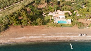 An aerial view of a coastal property with a swimming pool, a beach, and a boat. - Villa Pueblo (Nafplio)