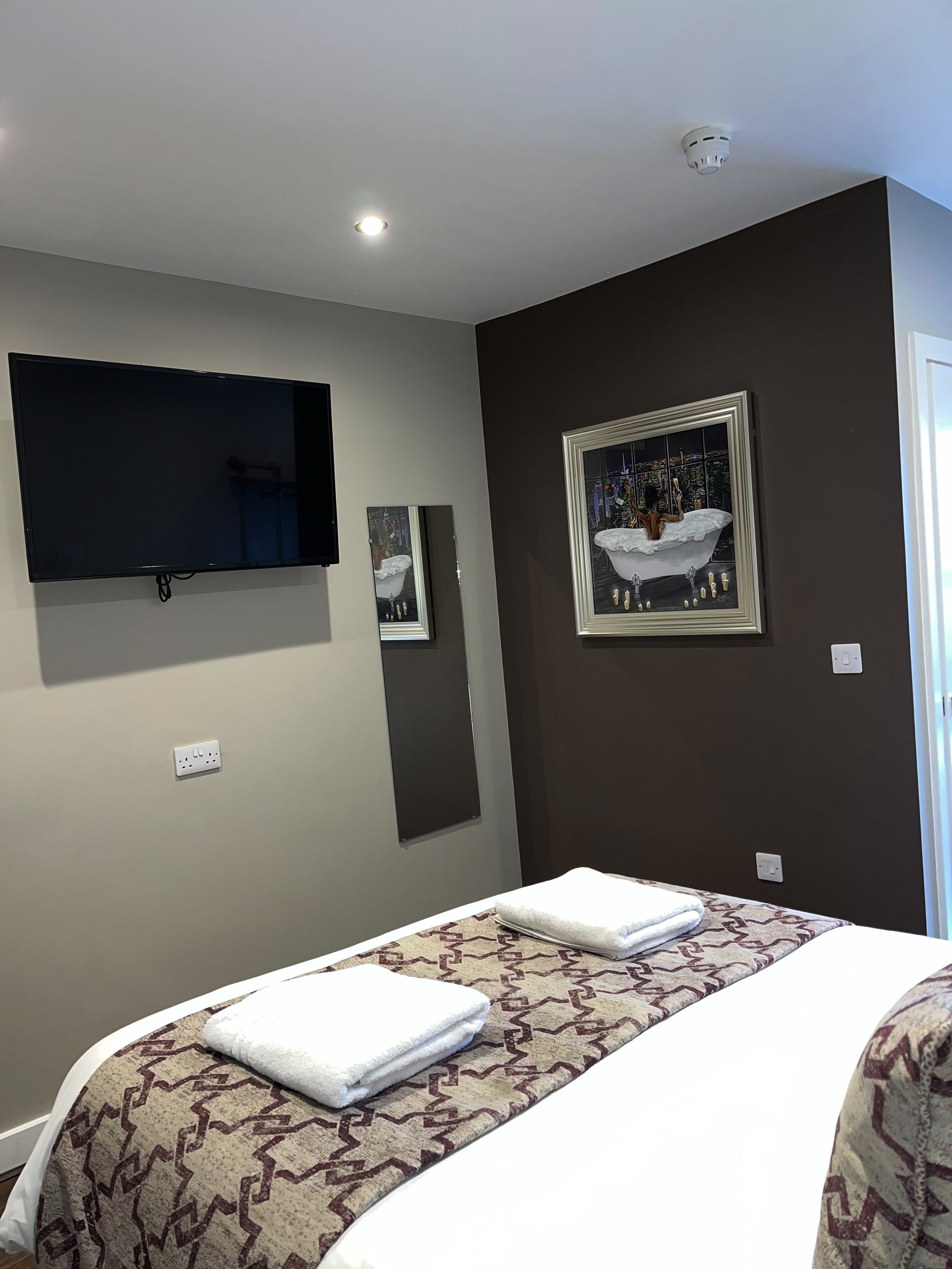 Ein Hotelzimmer mit Bett, einem an der Wand montierten Flachbildfernseher und einem gerahmten Kunstwerk, das eine Badeszene zeigt.