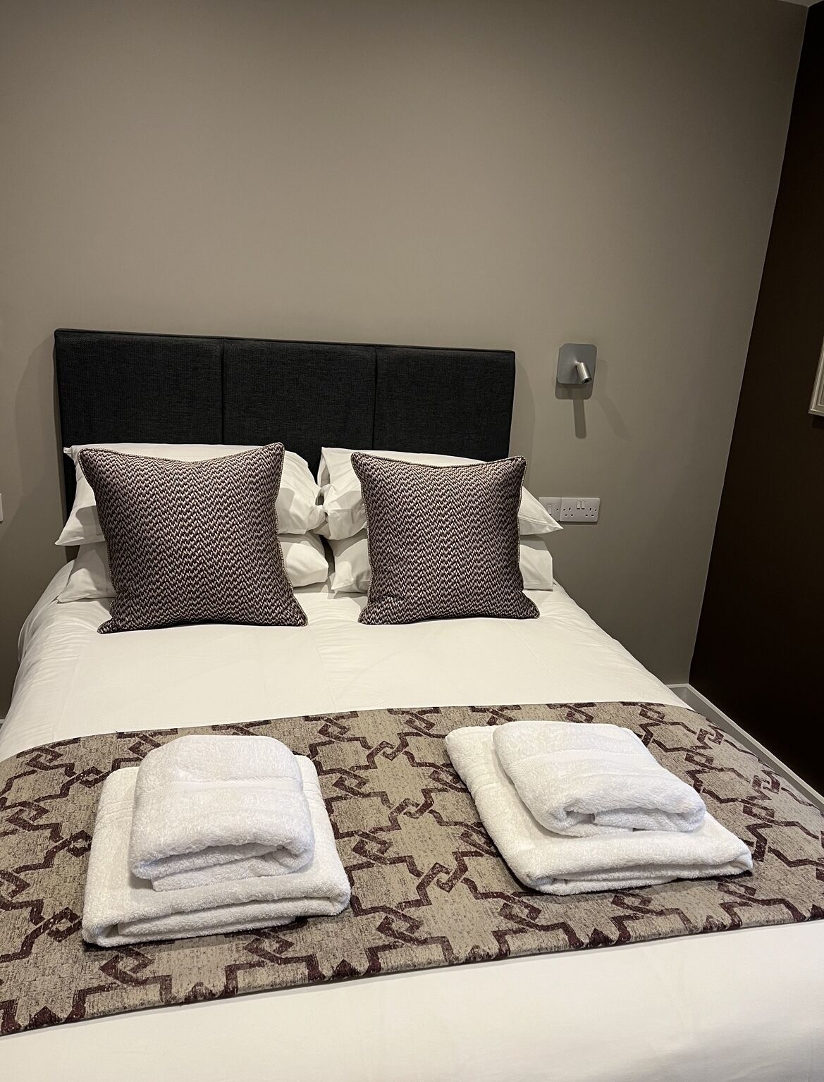 A neatly made bed with a patterned bedspread, two pillows, and two folded towels.