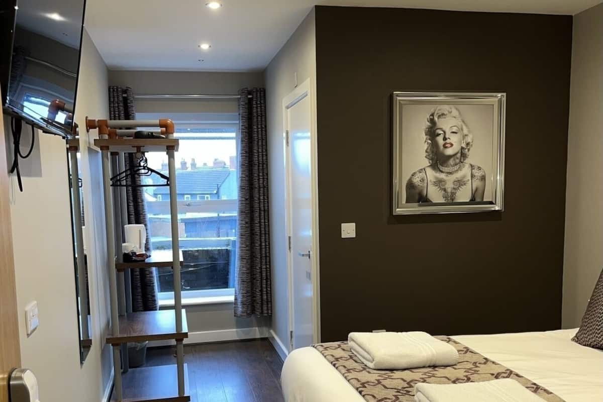 Hotelkamer met een bed, een wandtelevisie, een raam met gordijnen en een lijst met een afbeelding aan de muur.