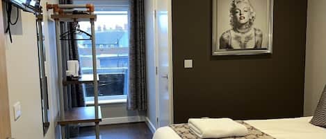 A hotel room with a bed, a mounted TV, a window with curtains, and a framed picture on the wall.