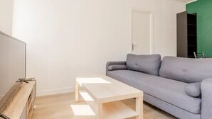 A minimalist living room with a grey sofa, a wooden coffee table, and a TV on a wooden stand.