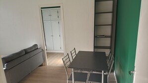 A room with a dark wooden table, four chairs, a grey sofa, and a white wardrobe.