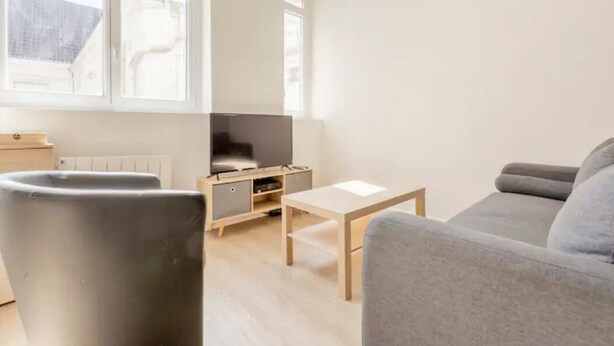 A modern living room with a grey sofa, a small wooden table, and a TV on a stand.