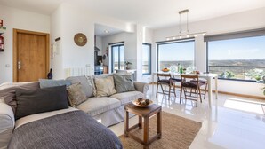 A modern living room with a sofa, a coffee table, and a dining area with a view.