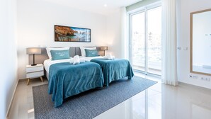 A modern hotel room with two beds, a large window, and a painting of a coastal scene. - Adega Marina Apartments - Urban View (Lagos)