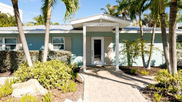 A house with a covered porch, palm trees, and a well-maintained garden. - Private Dock, Heated Pool & Beach Days (Holmes Beach)