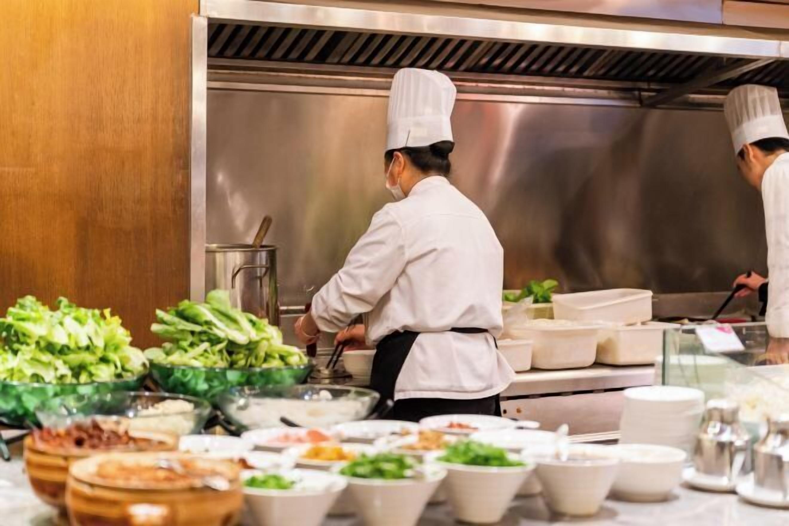 A chef preparing food in a professional kitchen with various dishes and ingredients visible.
