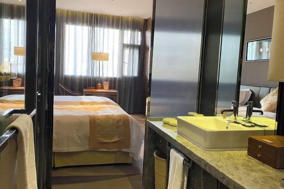 A hotel room with a bed, a bathroom with a sink, and a large window with curtains.