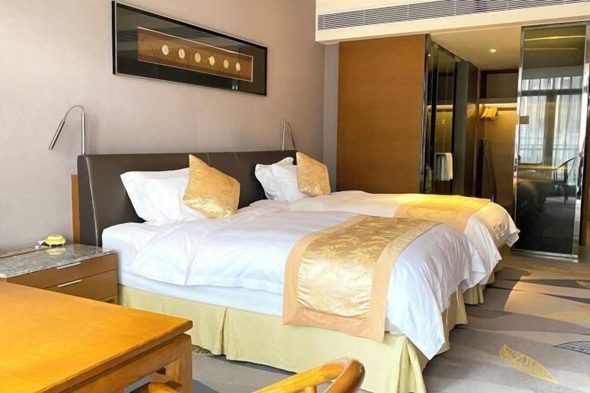 A hotel room with two beds, a desk, a chair, and a framed picture on the wall.