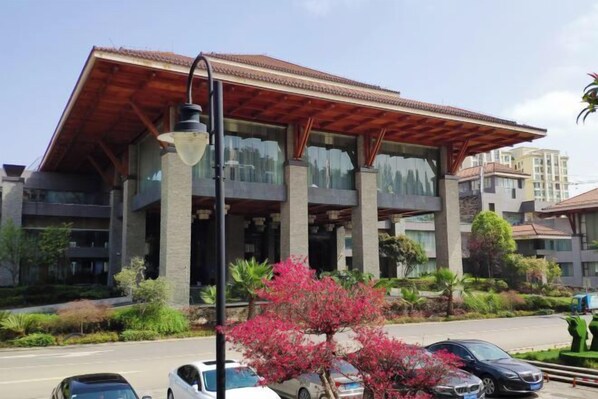 A modern building with a large glass facade, a covered entrance, and a parking area with cars.