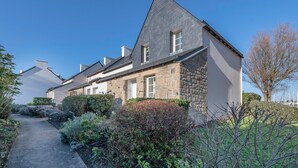 A stone building with a sloped roof, a pathway leading to the entrance, and a well-maintained garden with various shrubs and plants. - House for 6 - Cap sur l'Océan - Pool (Arzon)
