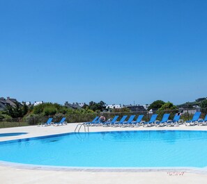 Une piscine avec des chaises longues bleues et un ciel dégagé.