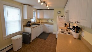 A compact kitchen with white cabinets, a sink, a stove, and a trash can. - Just 1.5 Blocks to the Beach and Boardwalk! (Rehoboth Beach)