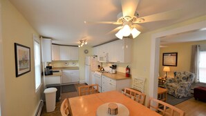 A compact kitchen with white cabinets, a microwave, and a stove. There is a dining table with chairs and a ceiling fan above. - Just 1.5 Blocks to the Beach and Boardwalk! (Rehoboth Beach)