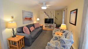 A living room with a grey sofa, a blue patterned sofa, a TV, and a ceiling fan. - Just 1.5 Blocks to the Beach and Boardwalk! (Rehoboth Beach)