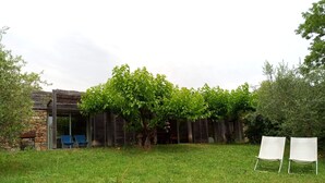 A rustic outdoor area with a stone wall, wooden pergola, and two white chairs. - 6/8 person gîte, all comforts in a family gîte village (Les Vans)
