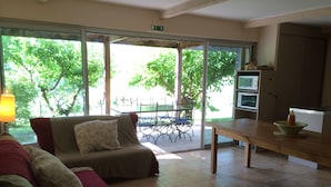 A living room with a sofa, a dining table, and a kitchen area with a microwave. - 6/8 person gîte, all comforts in a family gîte village (Les Vans)