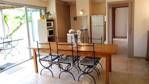 A dining area with a wooden table and black metal chairs, a kitchen with a refrigerator and microwave, and a door leading to a balcony with a view of greenery. - 6/8 person gîte, all comforts in a family gîte village (Les Vans)