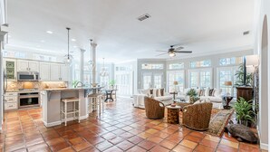 A spacious living area with a kitchen, large windows, and a ceiling fan. - Steps From the Beach ~ Golf Cart ~ Community Pool (Miramar Beach)