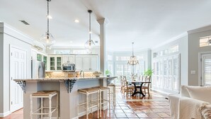 A spacious kitchen with white cabinetry, a central island with stools, and a dining area with a table and chairs. - Steps From the Beach ~ Golf Cart ~ Community Pool (Miramar Beach)